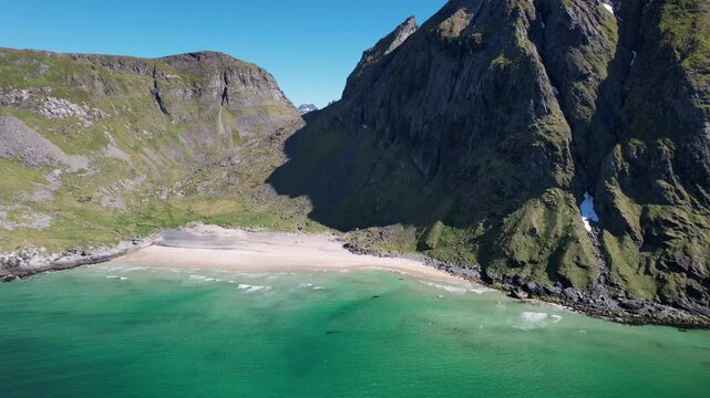 Breathtaking aerial footage moving backwards over the secluded Kvalvika beach, revealing majestic mountains and clear turquoise Arctic waters