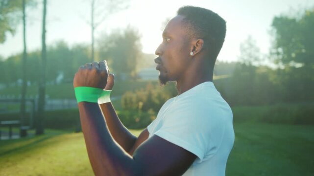 Morning resistance band exercise in park, Muscular male performing shoulder press outdoors at sunrise with band