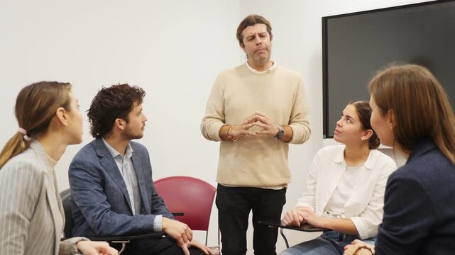 Middle-aged male teacher near interactive board explaining rules to group of students in classroom. Concept of studying of foreign language