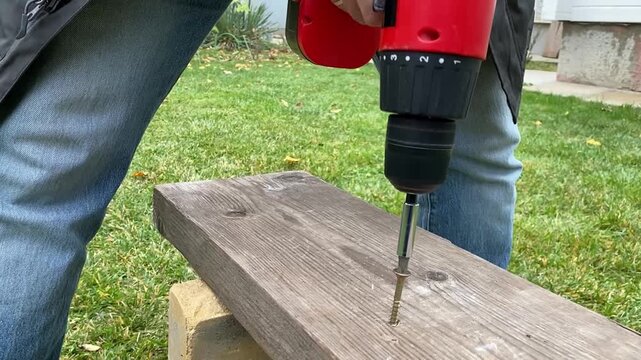 close up of cordless screwdriver pulling screw out of wooden board reverse rotation diy repair and disassembly process power tool in action workshop detail shot