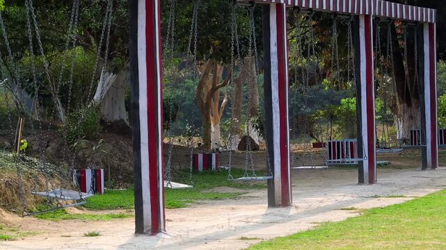 Row of empty swings in park with trees and greenery