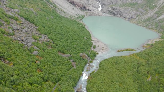 Drohnenflug mit tilt shot auf den Briksdalsbreen Gletscher &uuml;ber einem Gletschersee umgeben von Berggipfeln, bei Regenwetter. Felsige und Waldliche Umgebung. Raw unbearbeitet