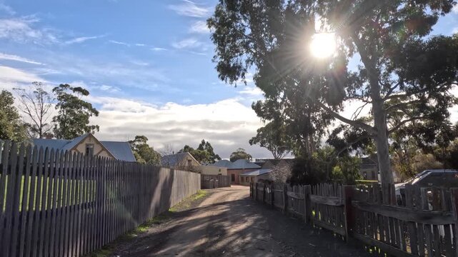 Driving down a dirt road past wooden fences and old buildings on a sunny day.