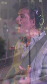 Vertical video: Camera moving revealing road bokeh over male singer at mic, singing for recording