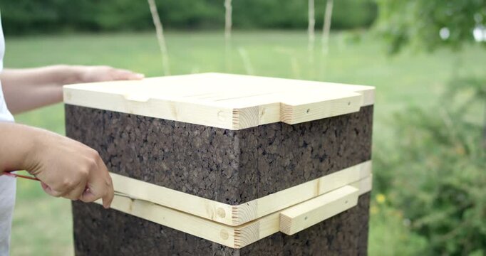 Person using a metal tool to carefully open a modern sustainable beehive made of cork and wood