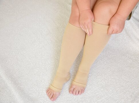 Women's legs in beige compression stockings. Prevents varicose veins, supports blood vessels, and improves circulation.Indispensable for long trips.