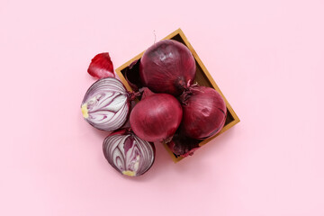 Wooden box with fresh red onions on pink background