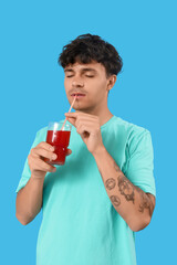 Fototapeta premium Young man drinking red juice on blue background