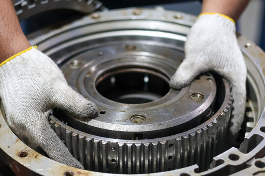 Mechanic hands installing a heavy planetary gear carrier into an automatic transmission housing during a professional gearbox rebuild and maintenance service.
