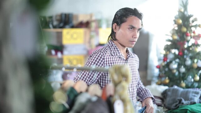 In chain shop, Indonesian man choose trousers, X mas shopping. Changing wardrobe, shaping style of clothing. Designer clothes, clothing of world brands. Modern urban fashion, casual practical clothes 