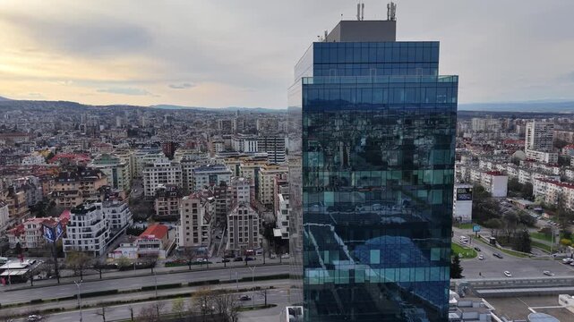 Aerial shot of a modern glass office building in a dense urban city environment.