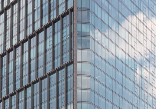 the sharp, angular convergence of a modern glass facade. Deep bronze mullions create a rigid grid that contrasts with the ethereal transparency of the windows, where the sky is mirrored in soft, paint
