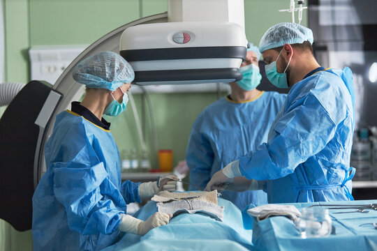 Wide shot of surgeons performing minimally invasive procedure in operating room with imaging equipment, supporting healthcare teamwork and modern treatment marketing use