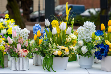 Naklejka premium Spring floral arrangements in pots at outdoor market, colorful Easter flower compositions with tulips and hyacinths, artisan holiday table decorations, high-quality artificial flowers for home decor, 