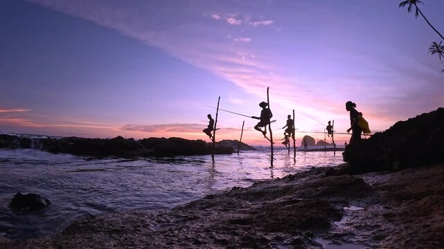 Sri Lankan stilt fishermen sitting on pole fishing at sunset in silhouette during dusk southern coast in Sri Lanka