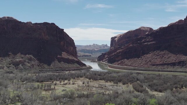 Colorado River approaching Moonflower Canyon near Moab Utah United States with Potash Road UT279 and Kane Springs Boulevard tracing canyon base between red sandstone cliffs, slow forward drone reveal