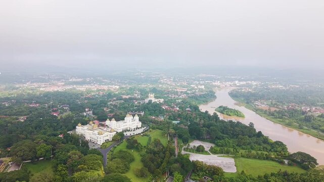 Aerial view of Kuala Kangsar in Perak, Malaysia, featuring Ubudiah Mosque and Istana Iskandariah surrounded by lush greenery and river landscape in soft atmospheric conditions. UHD.