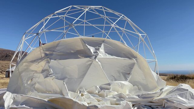 White geodesic dome frame partially covered with canvas in a dry landscape