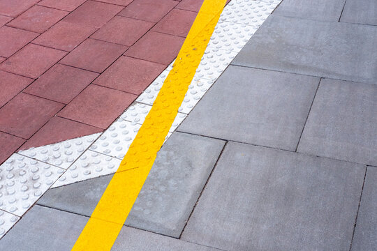 Closeup detail of tactile urban sidewalk pavement texture with yellow line marking highlighting safety cues in contemporary city infrastructure