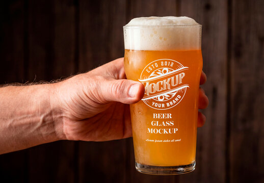 Hand holding glass of cold beer with foam against dark background
