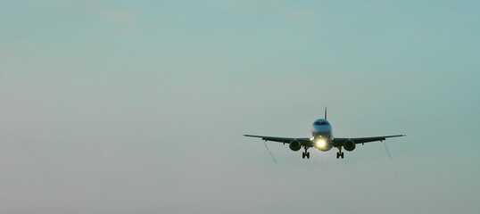Fototapeta premium Front side view commercial passenger aircraft or cargo transportation airplane flying on blue sky over sea and spread the wheel prepare landing to airport in cloudy sunset evening sky