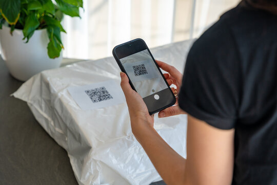 Person scanning QR code on parcel with smartphone camera for delivery tracking at home. Contactless technology mobile app and digital service concept.