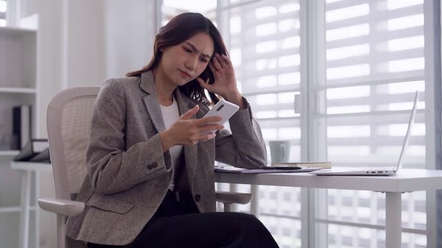 Asian adult woman experiencing stress worry frustration using smartphone dealing digital problem challenging situation modern workspace
