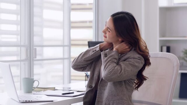 Asian woman experiencing neck shoulder pain stretching modern office desk workplace professional discomfort fatigue stress relief employee wellness