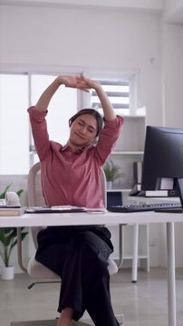 Asian adult woman professional worker stretching arms overhead relaxing at bright modern home office desk improving posture combating fatigue during remote work