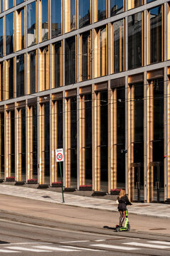 Child on scooter crossing an urban Oslo Norway street with modern architecture as sunlight highlights a safe everyday commute moment