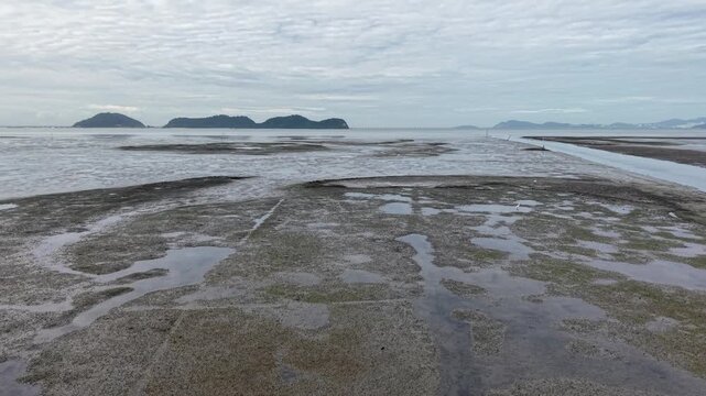Aerial view of exposed coastal mudflats at low tide with tidal pools and distant islands.