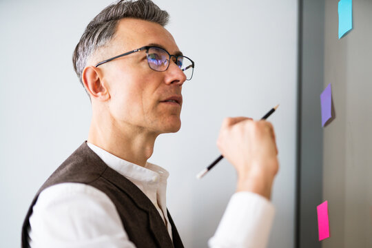 Worker engaged in planning and organizing ideas using colorful sticky notes on a wall during a brainstorming session in an office