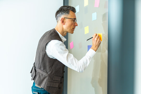 Man writes on sticky notes on a wall during a brainstorming session in an office space