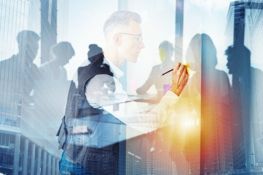Business meeting with team member writing on glass board in city office during daylight hours