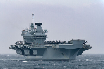 Royal Navy aircraft carrier HMS Prince of Wales sailing in Tokyo Bay, Japan, with F-35B fighter jets on deck, rough and cloudy weather. © zapper