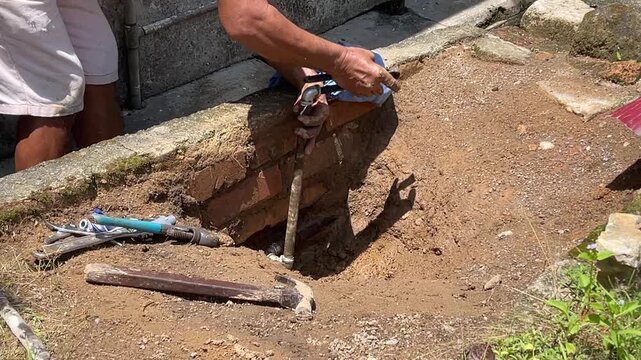 A man's hands using a professional Buteline clamp tool to rotate and adjust a metal pipe connector during a DIY home repair project outdoors.