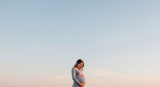 Pregnant Woman Holding Belly Outdoors at Sunset, Soft Sky Background