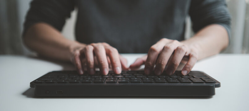 Close-up of a person typing on a black wireless keyboard at a desk. Professional developer or writer working on computer code or digital content