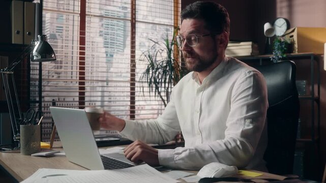 Tired Caucasian businessman yawning working laptop indoors office drinking coffee sleepy exhausted male business man worker overworked manager trader employee fatigue CEO burnout work online tiredness