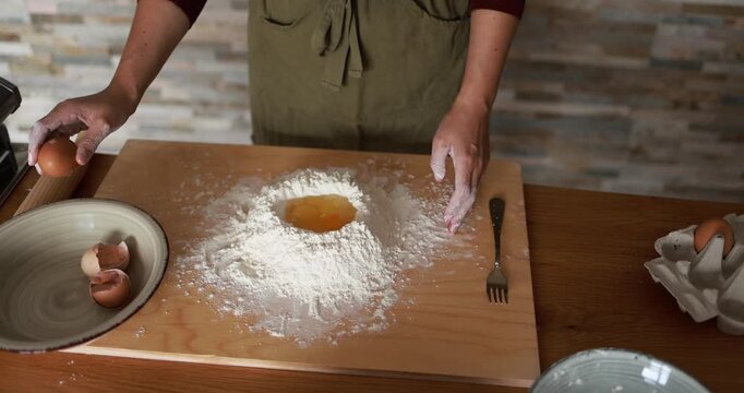 Woman preparing dough with flour and eggs for homemade pasta indoor - Italian food, culture and lifestyle concept