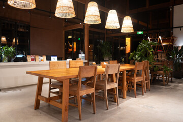 Wooden long table with wicker pendant lamps in a modern café interior at night