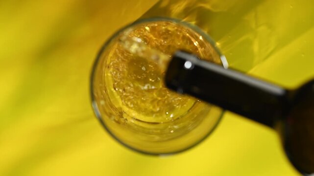A bottle pouring beer into a glass, creating bubbles, viewed from above. Concept of refreshment, advertising content for bars, pub, cafes, and restaurants, celebration, nightlife and social gatherings
