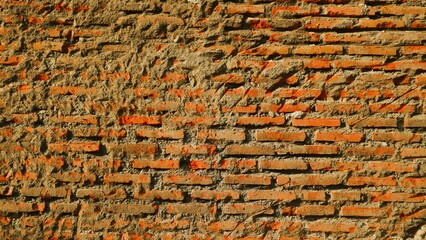 Close-up view of an old, weathered brick wall with rough texture and visible mortar, showing signs of age and decay under sunlight. © Wahjoekris