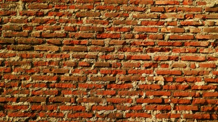 A close-up, textured view of an old, weathered red brick wall with visible mortar joints. © Wahjoekris