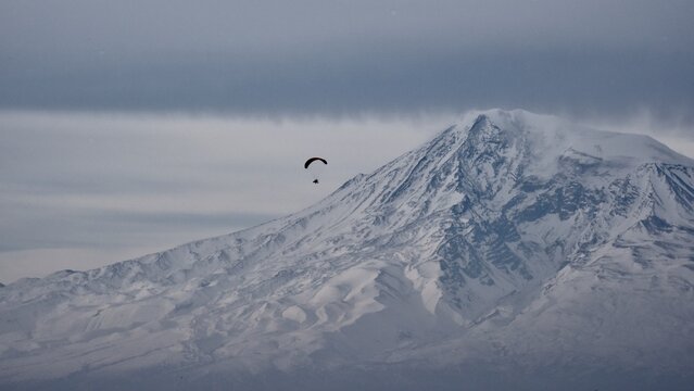 A paraglider flying against the massive snowy slopes of Mount Ararat, epic scale