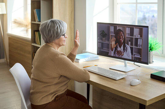 Doctor and senior woman telemedicine video consultation online. An elderly patient greets a doctor on a computer during a remote care call from home. Modern telehealth for seniors at home.