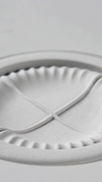 Vertical video: Tapping, pressing right fingertip creating pleats on white soft disc on gray table