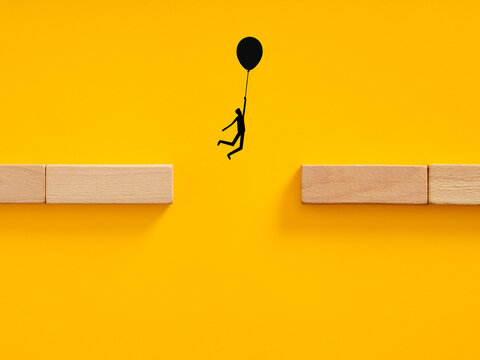 Person flying across gap with balloon, overcoming obstacle