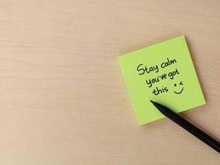 Obraz premium Stay calm you’ve got this message on green sticky note on wooden desk. Concept for mental health, workplace productivity, exam preparation, and positive mindset