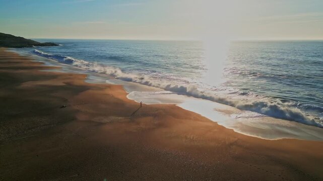 Sunlit beach at sunrise, waves gently hitting the shore in Salgado, Portugal